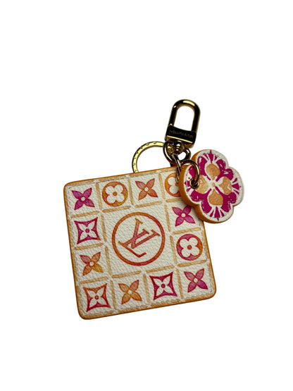 Louis Vuitton white square keychain with a pink and orange "LV" logo in the center surrounded by pink and orange monogram floral pattern.  There is also a pink and orange smaller flower keychain and both are attached to a gold key ring.