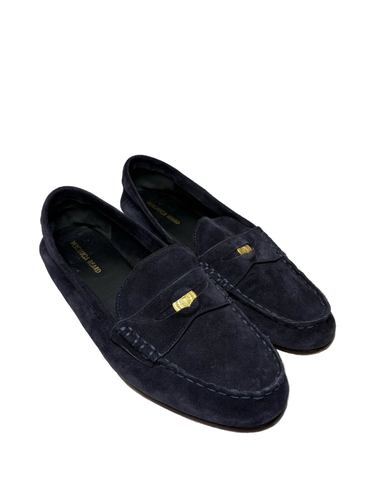 Dark blue suede loafers with a gold coin detail on a white backdrop