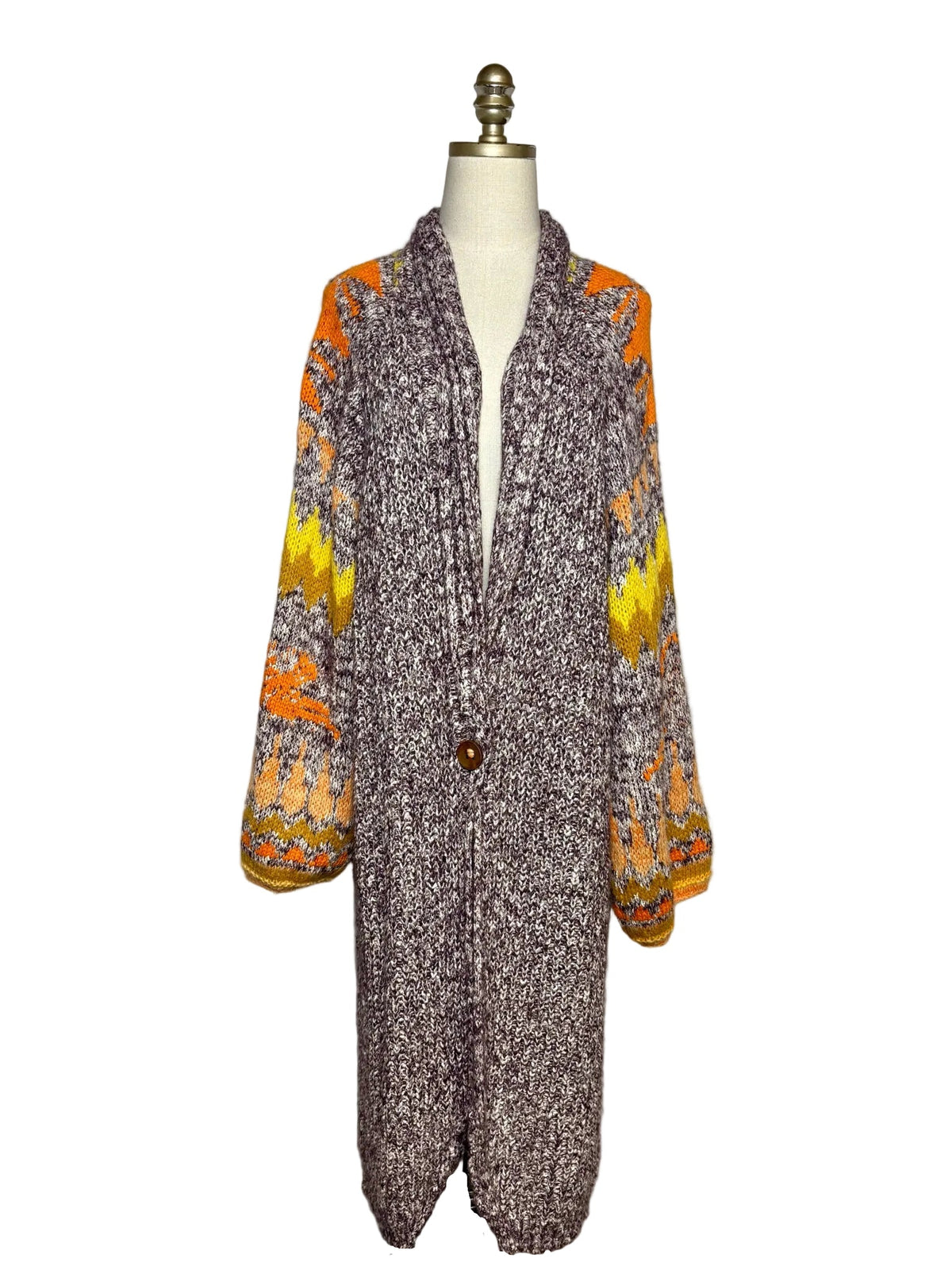 Long grey and brown sweater with one brown button and orange and yellow designs on the sleeves.  The sweater is on a mannequin in front of a white background